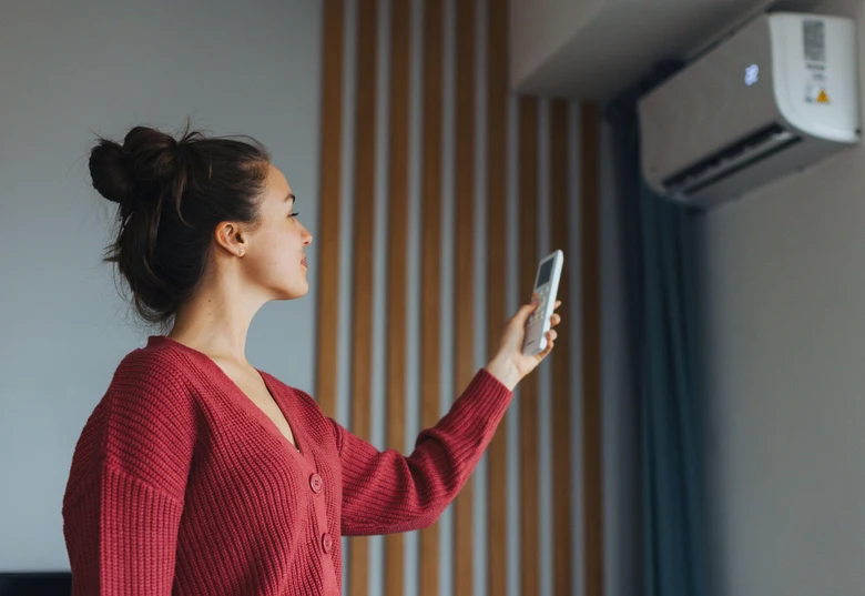 Žena ovládá klimatizaci mobilním telefonem v interiéru.