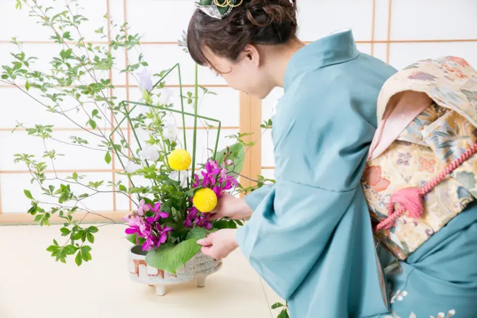Žena v kimónu aranžuje květiny ve stylu ikebana.