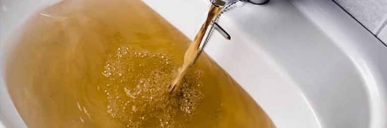 Zbarvená voda tekoucí z kohoutku do umyvadla