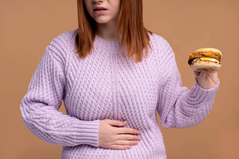 Žena drží burger a dotýká se břicha, pocit plného žaludku