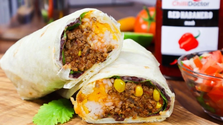 Dva nakrájené burrito s rýží, fazolími a masem na dřevěném talíři.