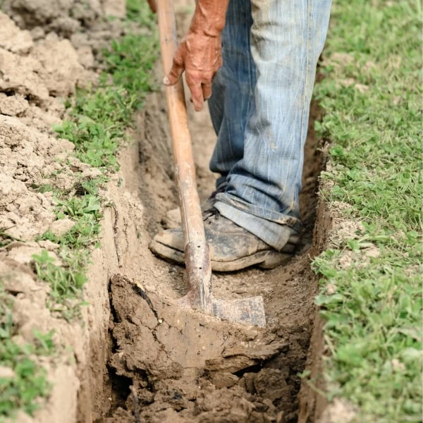 Muž kopáčem kopává příkop pro drenáž