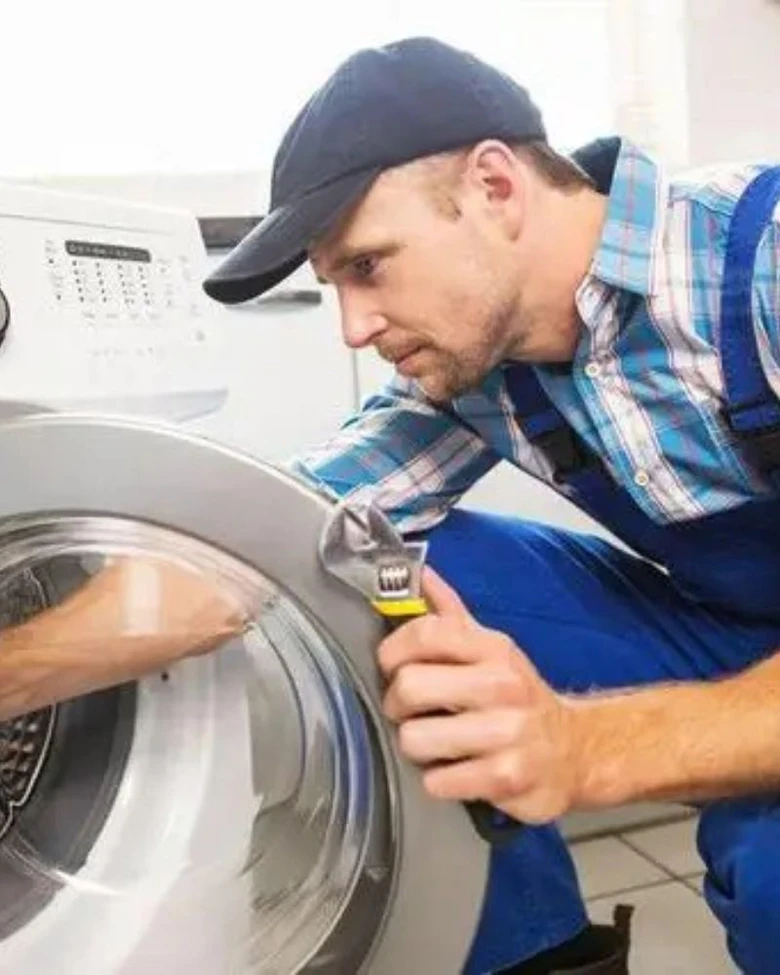 Technik opravuje pračku pomocí klíčového nástroje.