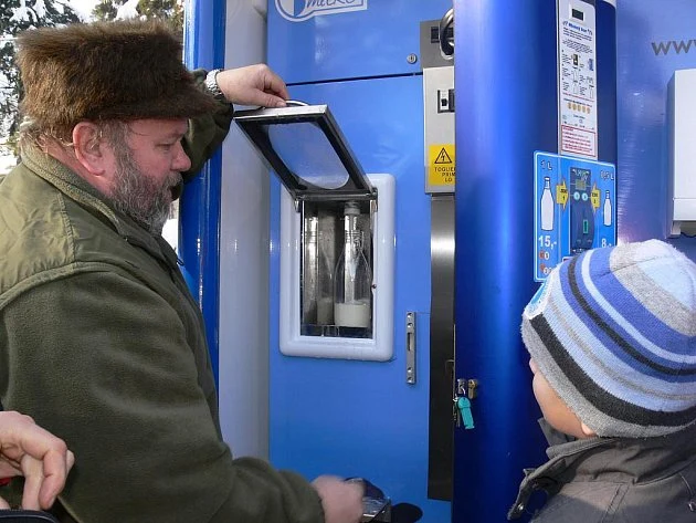 Muž nalévá syrové mléko z modrého automatu venku.