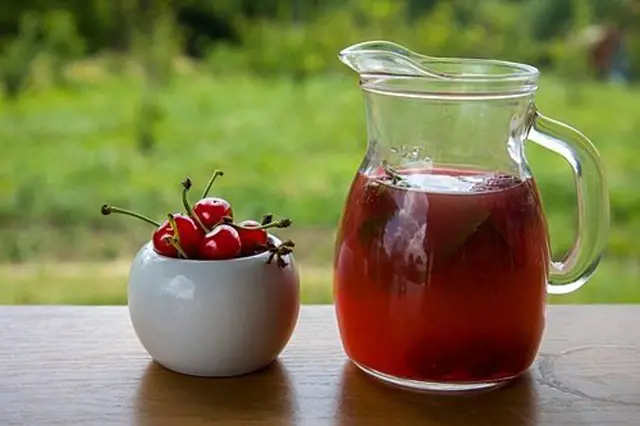 Sklenice třešňové šťávy s čerstvými třešněmi vedle ní.