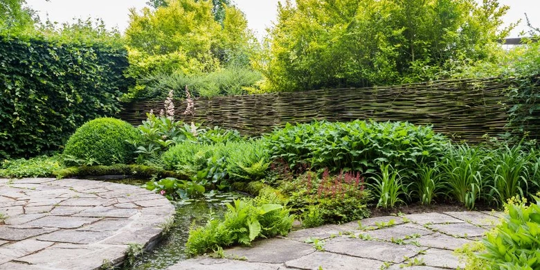 Permakulturní zahrada s kamenitou cestou a bohatou vegetací.