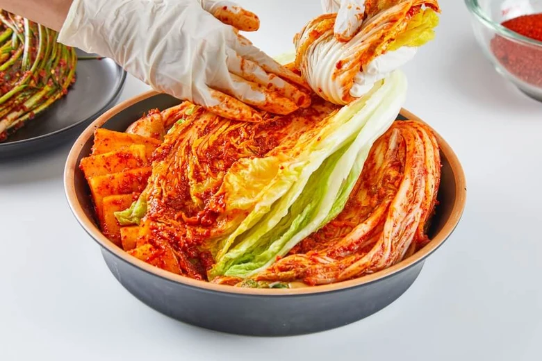 Ruce mazají červenou omáčku na listy zelí pro kimbap.