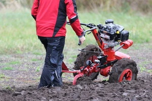 Farmař připravuje půdu pro pěstování brambor pomocí motokultivátoru.