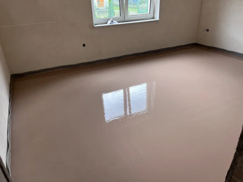 Nová podlaha z anhydritu v prázdné místnosti s odrazem okna.