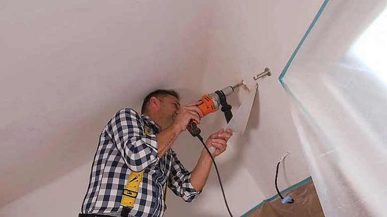 Muž odstraňuje potrubí přes zeď pomocí vrtáku