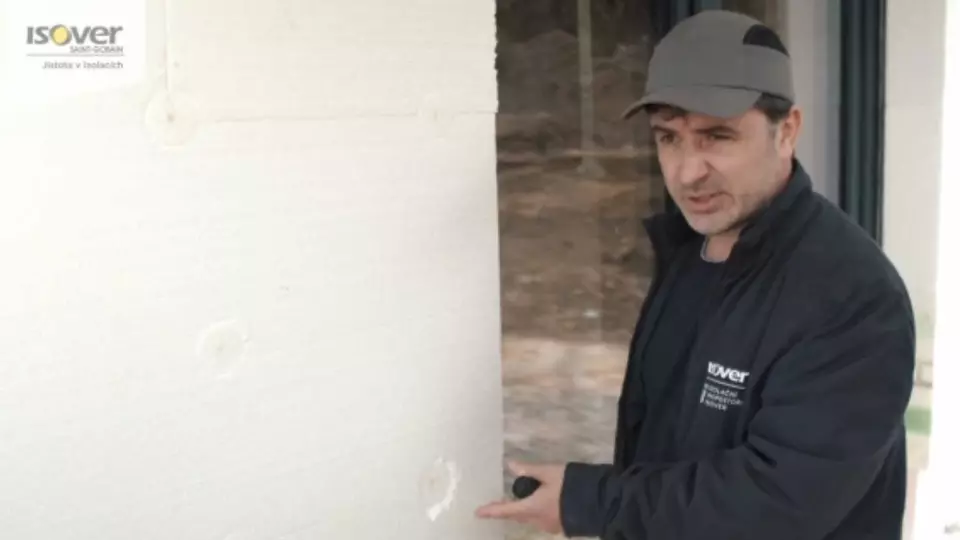 Muž ukazuje kotvení polystyrenové izolace na fasádě