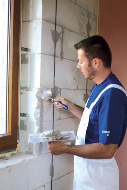 Muž aplikuje vnitřní špaletu kolem okna