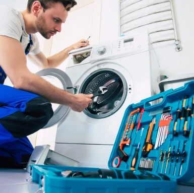 Mechanik opravuje pračku s nářadím v modrém kufru.