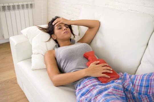 Žena s horkou fľaškou na břiše při menstruačních potížích