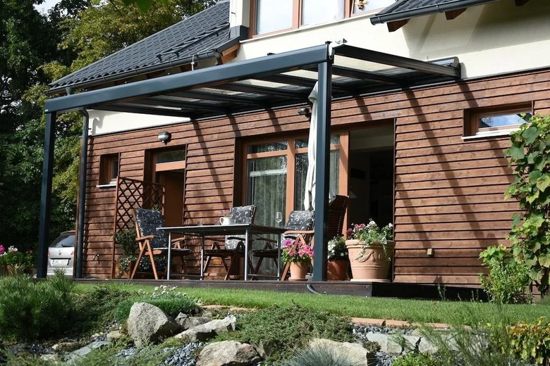 Moderní pergola připevněná k fasádě domu s zahradním nábytkem.