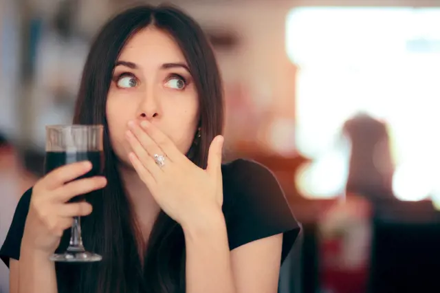 Žena s nápojem zakrývá ústa rukou po říhání.