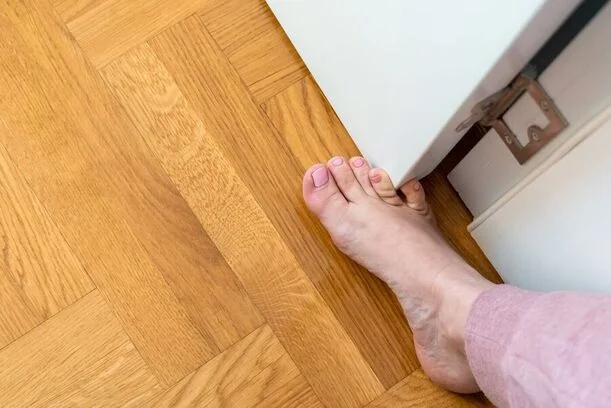 Holá lidská noha na dřevěné podlaze u dveří.