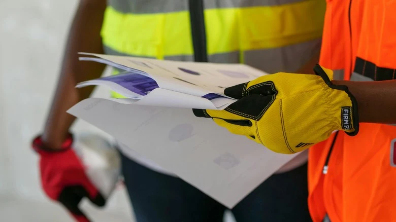 Stavební dělníci s plány v rukou při kontrole dokumentace.