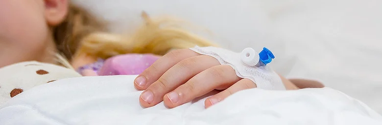 Dětská ruka s infuzní jehlou v nemocničním lůžku.