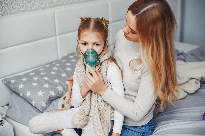 Matka pomáhá dceři s inhalací pomocí rozprašovače pro suchý kašel.