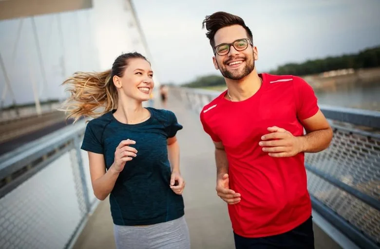 Muž a žena běží po mostě v sportovním oblečení.