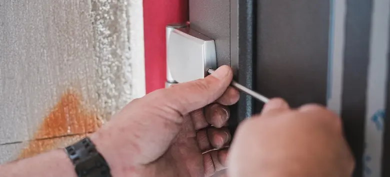 Ruka s šroubovákem upravuje zámek plastových dveří