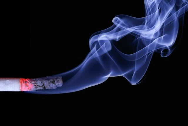 Zapálený cigaret s kouřem na černém pozadí