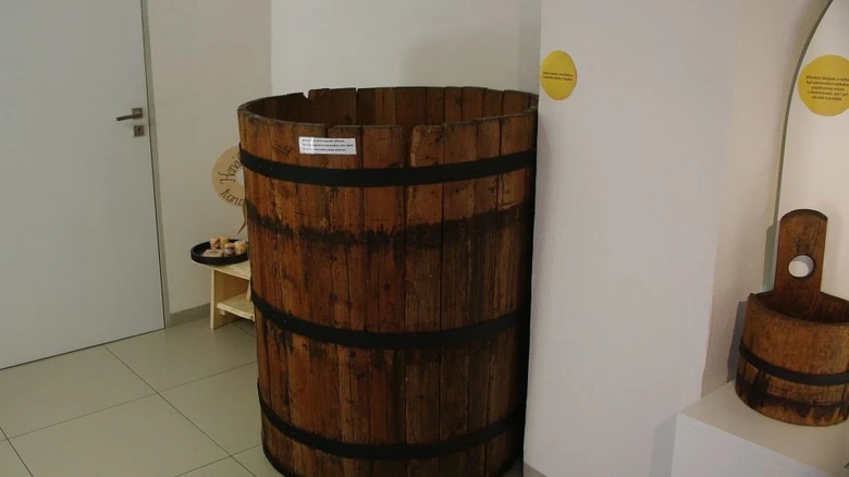 Velký dřevěný barel v expozici muzea s menšími nádobami.