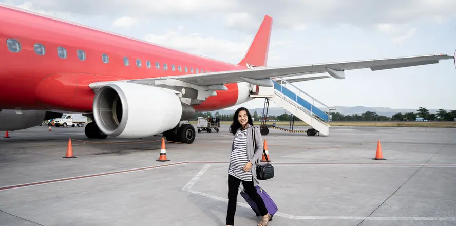 Pregnant woman with luggage near airplane