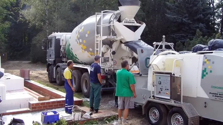 Stavebníci s betonovou směšovačkou na terénním staveništi.