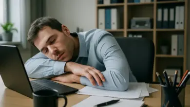 Unavený muž spí za pracovištěm s otevřeným počítačem.
