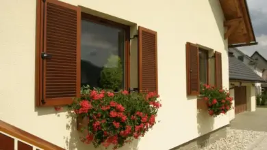 Venkovní okenice na domě s kvetoucími okenními boxy.