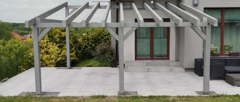 Nově postavená dřevěná zahradní pergola na dlažbě u domu.