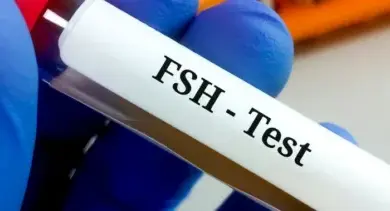 Krevní vzorek s nápisem FSH-test držaný rukou v modrých gumových rukavicích.