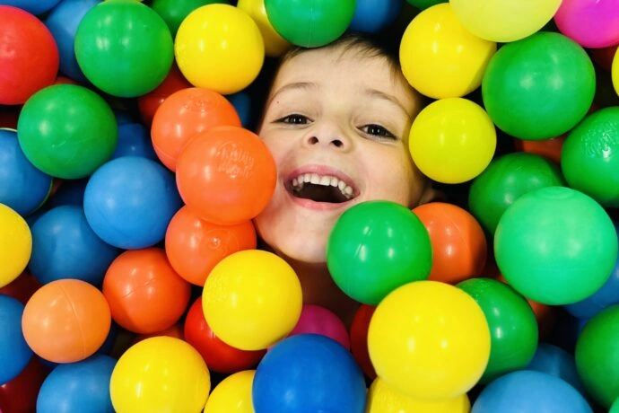 Dítě v barevných plastových koulích na hřišti.