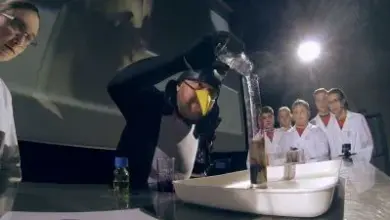 Učitel demonstruje chemický pokus před skupinou studentů.