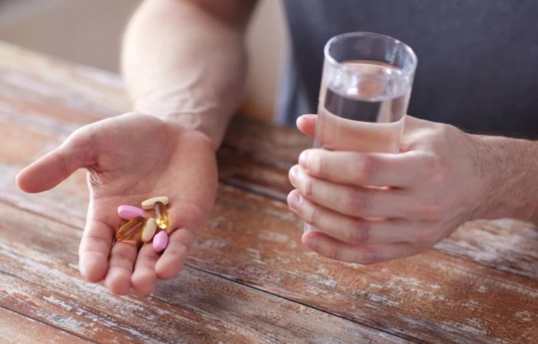 Ruce sportovce s vitamíny a sklenicí vody na dřevě.