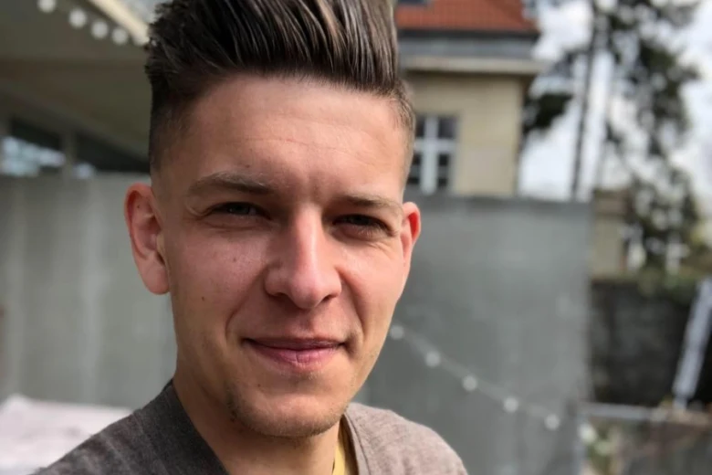 Mladý muž se usmívá venku před domem.