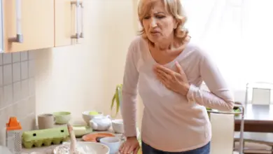 Žena v kuchyni drží ruku na hrudi kvůli bolesti při infarktu.