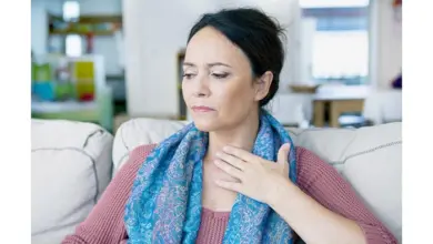 Žena sedí na gauči s bolestmi v krku nebo chrapotem.