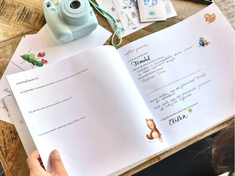 Otevřená kniha s českými jmény pro dítě vedle fotoaparátu.