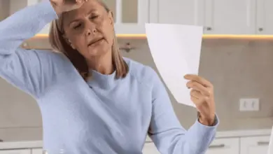 Žena sedící u stolu s dokumentem vypadá unaveně nebo má horké vlny.
