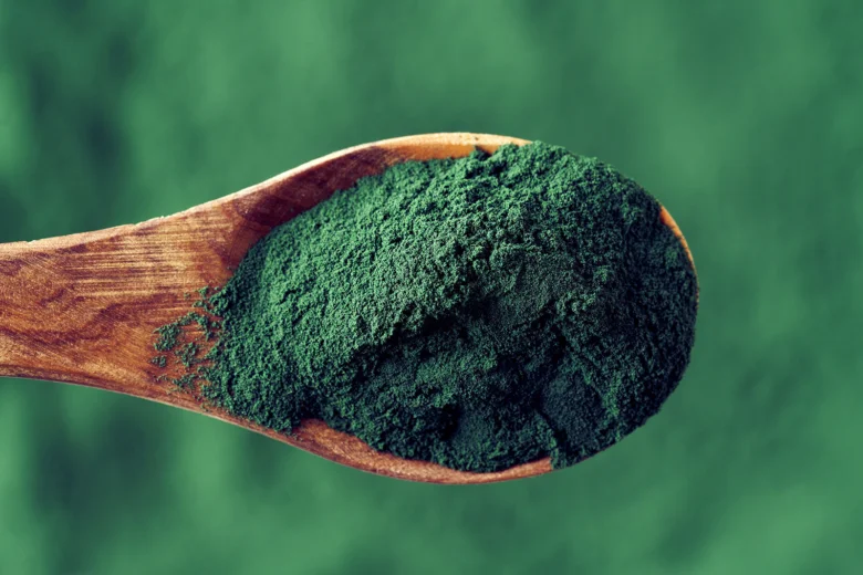 Dřevěná lžička plná zeleného prášku z řasy Spirulina.