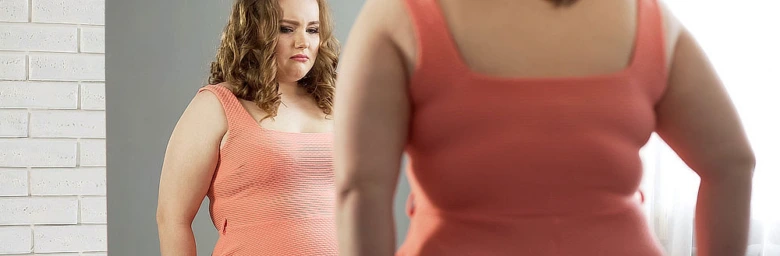 Žena v oranžovém tričku se dívá do zrcadla.