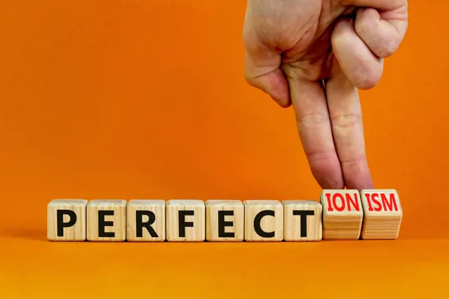 Ruka odstraňuje slovo 'IONISM' ze slov 'PERFECT', ilustrující perfekcionismus.