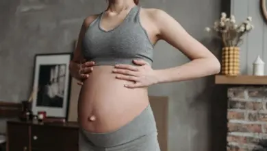 Těhotná žena s rukama na břiše v domácnosti.