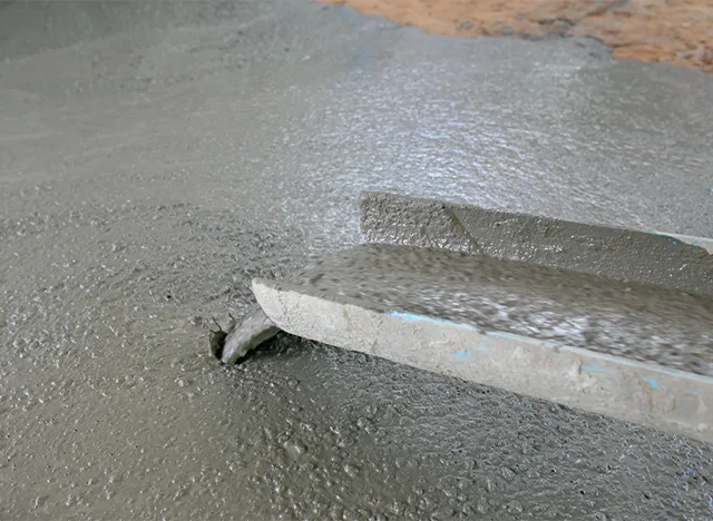 Mokrý beton se hladí ručním špachtlou na podlaze.