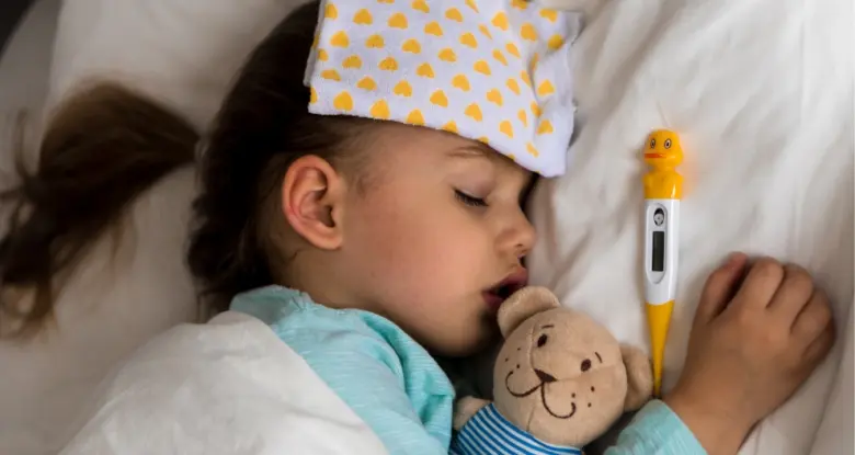 Spící nemocné dítě s teploměrem a polštářem na čele.