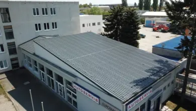 Bílá budova s pultovou střechou z kovu na průmyslovém areálu.