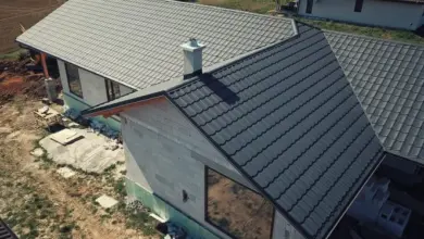 Střecha novostavby s šedými taškami na pozadí nezpevněného terénu.